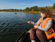 © Pavel Losevsky - Woman in an orange life jacket is fishing in a boat. She is holding a fishing pole and has a fish on it