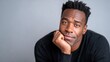 © evgenia_lo - A Black man in his 40s rests his chin on his knuckles while posing in a studio. He wears a simple black long-sleeve top with soft diffused lighting