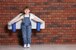 © New Africa - Little girl with cardboard plane wings playing pilot near brick wall, space for text