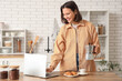 © Pixel-Shot - Beautiful young woman with geyser coffee maker, croissants and laptop in kitchen