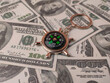 © Mohd Azrin - small metal compass keychain resting on a bed of US hundred-dollar bills