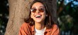© Z A C - Woman smiling outdoors, sunglasses, curly hair, casual attire.