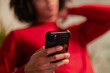 © Studio Marmellata - A person in a red top holds a smartphone, touching their neck with their other hand.