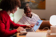 © Studio Marmellata - Two young men collaborate on a project using laptops at a table, illuminated by a warm desk lamp.