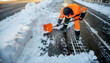 © justsann - Worker in orange uniform shoveling snow from a street.
