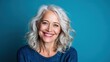 © Freshpixel - A cheerful older woman with wavy silver hair smiles warmly against a blue background, showcasing confidence and joy in her appearance and demeanor while embodying beauty.