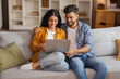 © Home-stock - Indian spouses relaxing with laptop on couch, embracing and using computer, browsing internet or shopping online together
