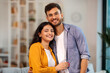 © Home-stock - Love and happiness. Portrait of Indian couple hugging and smiling to camera, standing in living room. Family moments concept