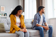 © Home-stock - Unhappy Indian spouses experiencing marriage crisis, sitting on different sofa sides in sulking silence after conflict, feeling upset after domestic quarrel