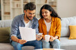 © Home-stock - Indian couple intently examining documents together, with cellphone, woman holding coffee mug, sitting on couch in living room