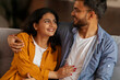 © Home-stock - Cheerful Indian lovers couple enjoying time together at home, embracing and talking, sitting on couch in living room. Love and relationship concept