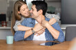 © fizkes - Young 30s couple spend time in cozy kitchen, embracing and looking at each other with love. Beautiful Latina woman hugging from behind her beloved man, expressing support, share warmth and affection