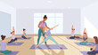© markusmiller - Yoga class with instructor assisting students in bright studio