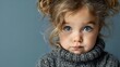 © Yuliia - Adorable blonde toddler girl with blue eyes wearing cozy gray knit sweater against soft blue background for children fashion and lifestyle content.