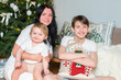 © Ruslan Russland - A family photo by the Christmas tree at home. A mother with her two teenage sons and a baby sit on the floor, posing for a photo in the living room before Christmas.