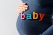 © dave - Close-up of expectant mother's belly spelling baby with wooden letters, clean white background. Perfect for healthcare, birth announcements, and family blogs.