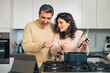 © Lomb - Authentic middle aged couple cooking together using online recipe on tablet in modern kitchen