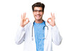 © luismolinero - Young doctor man over isolated background showing an ok sign with fingers