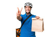 © luismolinero - Young caucasian man taking a bag of takeaway food over isolated background smiling and showing victory sign