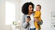 © Wool World - Happy mother holding her baby while looking at her smartphone at home.