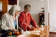 © Drobot Dean - Two female friends standing at a table laughing while one of them cuts carrots