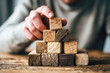 © Kowit - A hand stacking wooden blocks into a pyramid shape on a table, illustrating creativity and focus in play or construction.