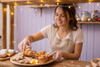 © smth.design - Smiling female baker arranging fresh pastries and festive cookies on wooden counter in cozy holiday kitchen with warm lights