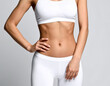 © Jakob - A close-up shows a toned female torso in white sportswear against a neutral background. The image focuses on fitness, body shape, and health.