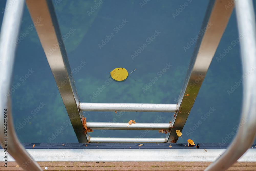 Metal handrail for descent into the lake, pier on the lake and calm lake water on background, selective focus