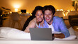 © Prostock-studio - Happy spouses are lying in bed, watching a comedy movie on a laptop. They are enjoying each other's company and having fun in the cozy atmosphere of their home in the evening.