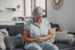 © Daniel - Elderly woman sits on a sofa at home holding her stomach, experiencing abdominal pain and discomfort. She looks tired and stressed while managing digestive issues during her daily life.