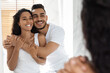 © Prostock-studio - A man and woman smile happily as they embrace each other in front of a mirror. The room is bright, creating a warm atmosphere in the afternoon light.
