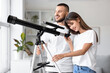 © Pixel-Shot - Young couple looking through telescope near window at home