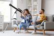 © Pixel-Shot - Young couple looking through telescope on sofa at home