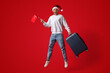 © Prostock-studio - A joyful traveler is jumping in the air while wearing a Christmas hat. He holds a suitcase in one hand and a small Turkish flag in the other, celebrating the holiday season.
