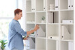 © Pixel-Shot - Young businessman taking folder from shelf in office