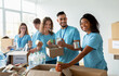 © Prostock-studio - A diverse group of volunteers smiles while sorting donated food at a community charity donation center. They prepare boxes filled with essentials for those in need.