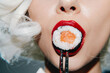 © VICHIZH - Close-up of a woman with red lips holding sushi with chopsticks, showcasing vibrant colors and a modern aesthetic, ideal for food and lifestyle concepts.
