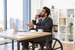 © sofiko14 - An Indian businessman in a wheelchair is talking on the phone while working in his office