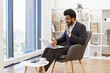 © sofiko14 - An Indian businessman gestures while participating in a video conference on his laptop in a modern office setting
