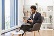 © sofiko14 - An Arab businessman gestures while participating in a video conference on his laptop in a modern office setting