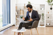 © sofiko14 - An Indian businessman is engaged in a video conference, using a laptop in a modern office setting