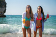 © NDABCREATIVITY - Two happy women toasting colorful beach drinks under the sun, enjoying tropical vibes and friendship