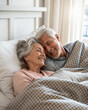 © Margo Miro - Elderly couple cuddling in bed under a blanket with smiles and affectionate expressions