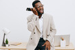 © SHOTPRIME STUDIO - Professional young African American man in smart casual attire talking on mobile phone while standing at office desk, working remotely, on white background. Business communication, technology, office