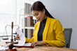 © Wasan - Legal advice concept. Female lawyer reviewing contract documents on wooden table in office.
