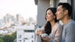 © Vyatcheslav - Happy Asian couple drinking coffee on a balcony with city view. Young man and woman holding mugs and looking at urban skyline. Romantic morning lifestyle concept