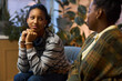 © DragonImages - Black teenage girl sitting with Black middle aged woman in office setting, teenager resting chin on hands and looking at woman, both engaged in conversation, plants in background
