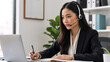 © Vyatcheslav - Asian call center agent with headset working in customer service. Professional woman consulting client online and taking notes at her desk