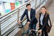 © DG PhotoStock - Business colleagues walking with bicycles along modern urban walkway while commuting to work. Sustainable transportation, eco friendly lifestyle, people commuting, teamwork, and modern city life.